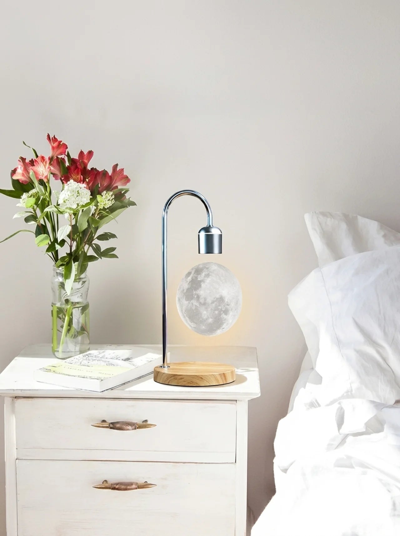 Lamp on a nightstand next to a vase of flowers in a bedroom setting